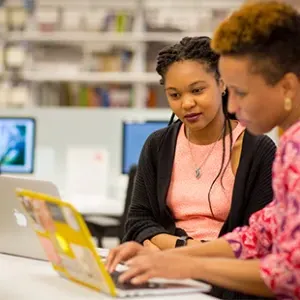 A student working on a laptop with a librarian